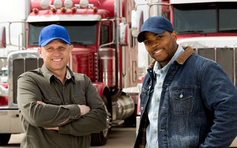 2 truck drivers stand in front of their truck